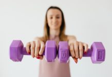 purple dumbbells in hands of positive sportswoman